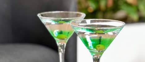 Two martini glasses on a marble table with a black bowl of nuts.