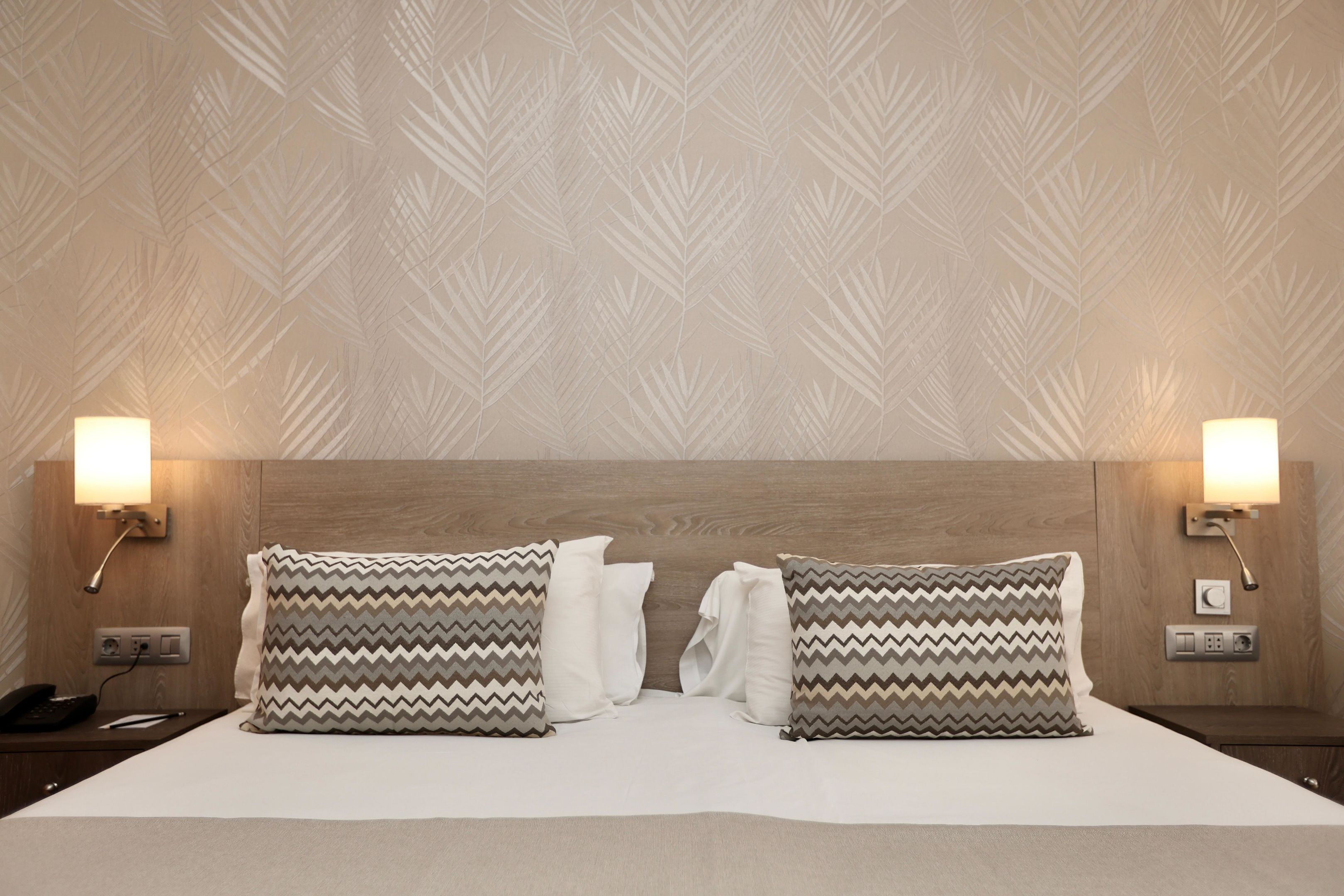Quarto de hotel com uma cama grande, duas mesas de cabeceira, um painel de cabeceira de madeira e luminárias fixadas na parede.