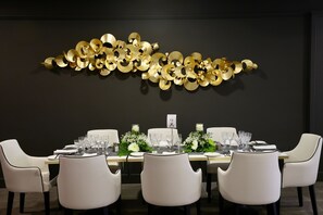 Une table à manger entourée de chaises blanches, un élément décoratif doré accroché au mur et un grand chiffre au mur.