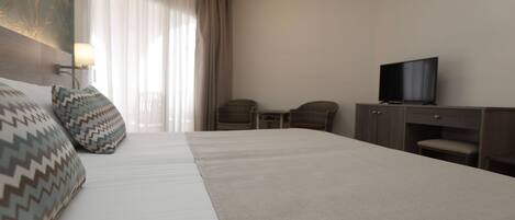 Una habitación de hotel con una cama grande, dos sillones, un escritorio con televisor y una ventana con cortinas.