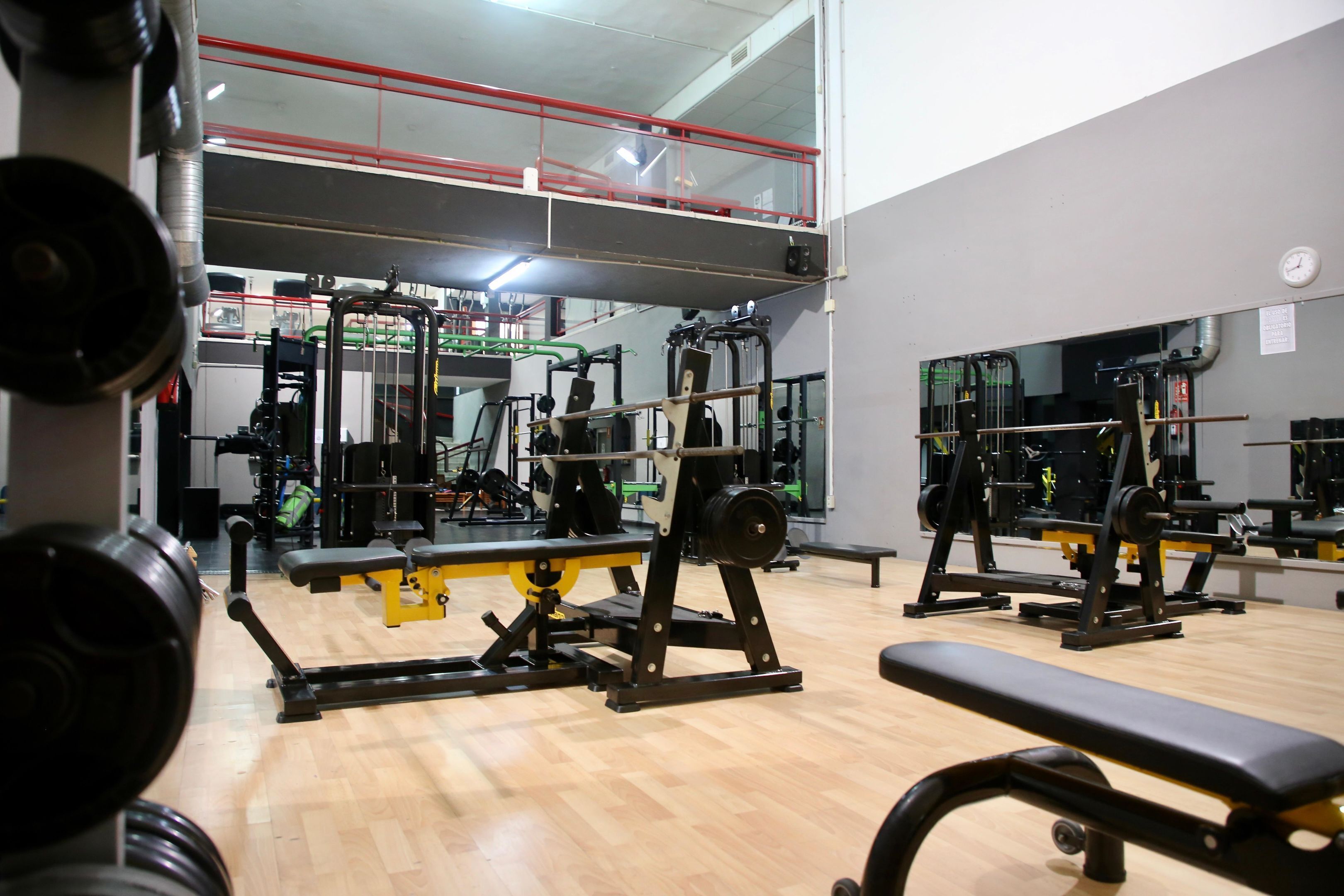 A gym with various exercise equipment, a wooden floor, and a red railing on an upper level.