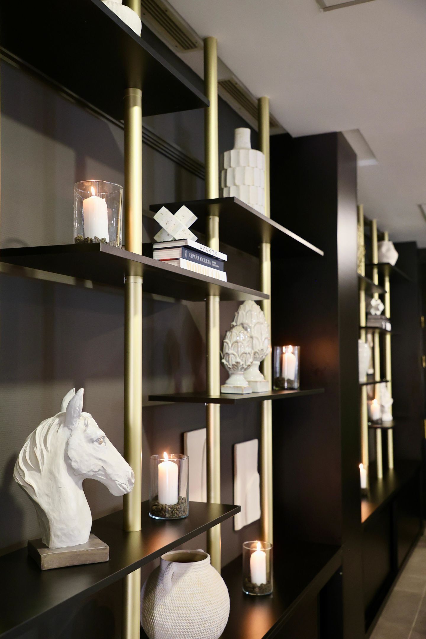 A modern interior with dark walls, gold shelving, and decorative items like candles and sculptures.