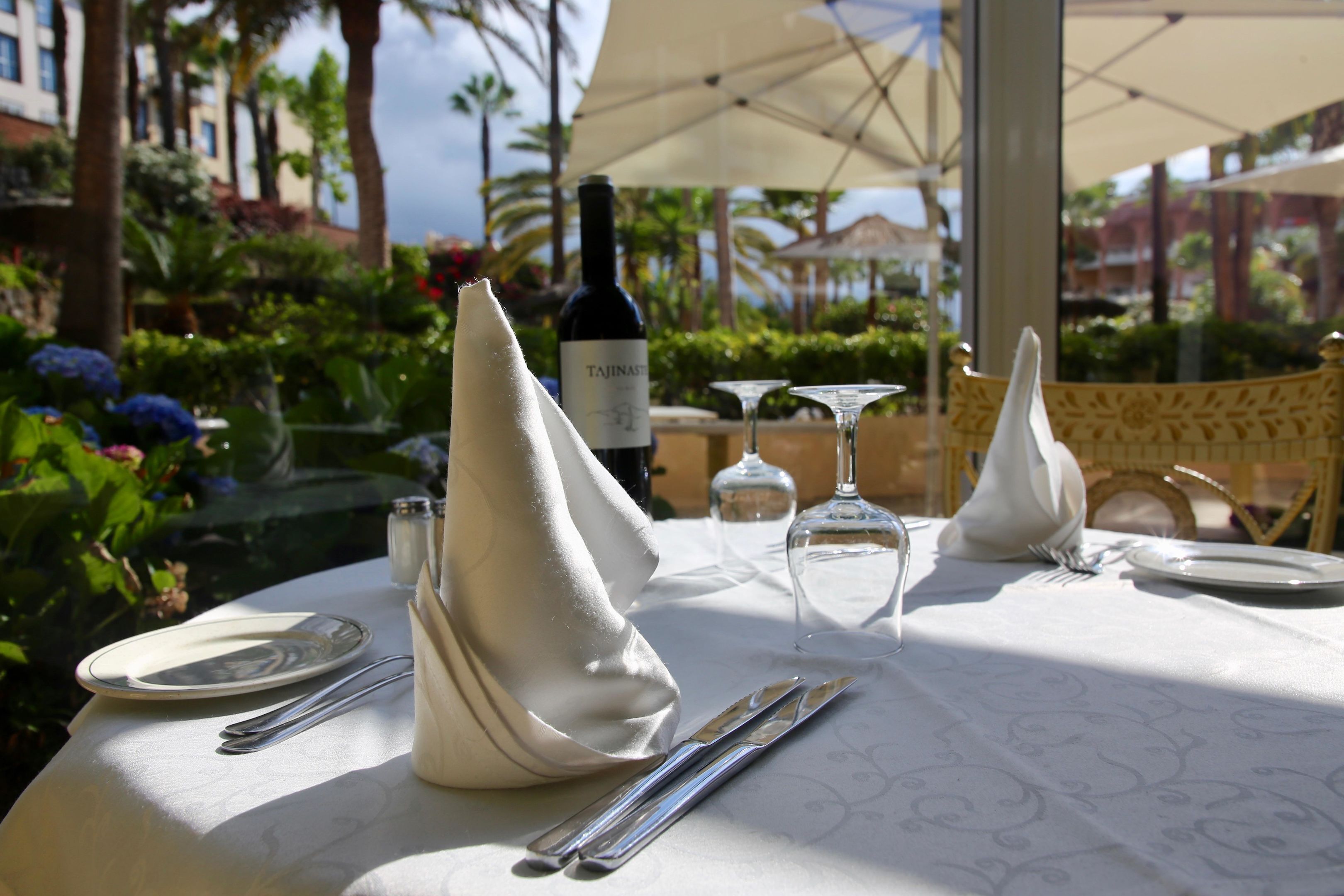 A table set for dining with a bottle of Tajin wine, two wine glasses, a folded napkin, and cutlery.