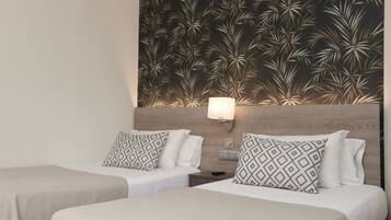 A hotel room with two beds, each with patterned pillows, a nightstand, a wall-mounted lamp, and a decorative wall panel.