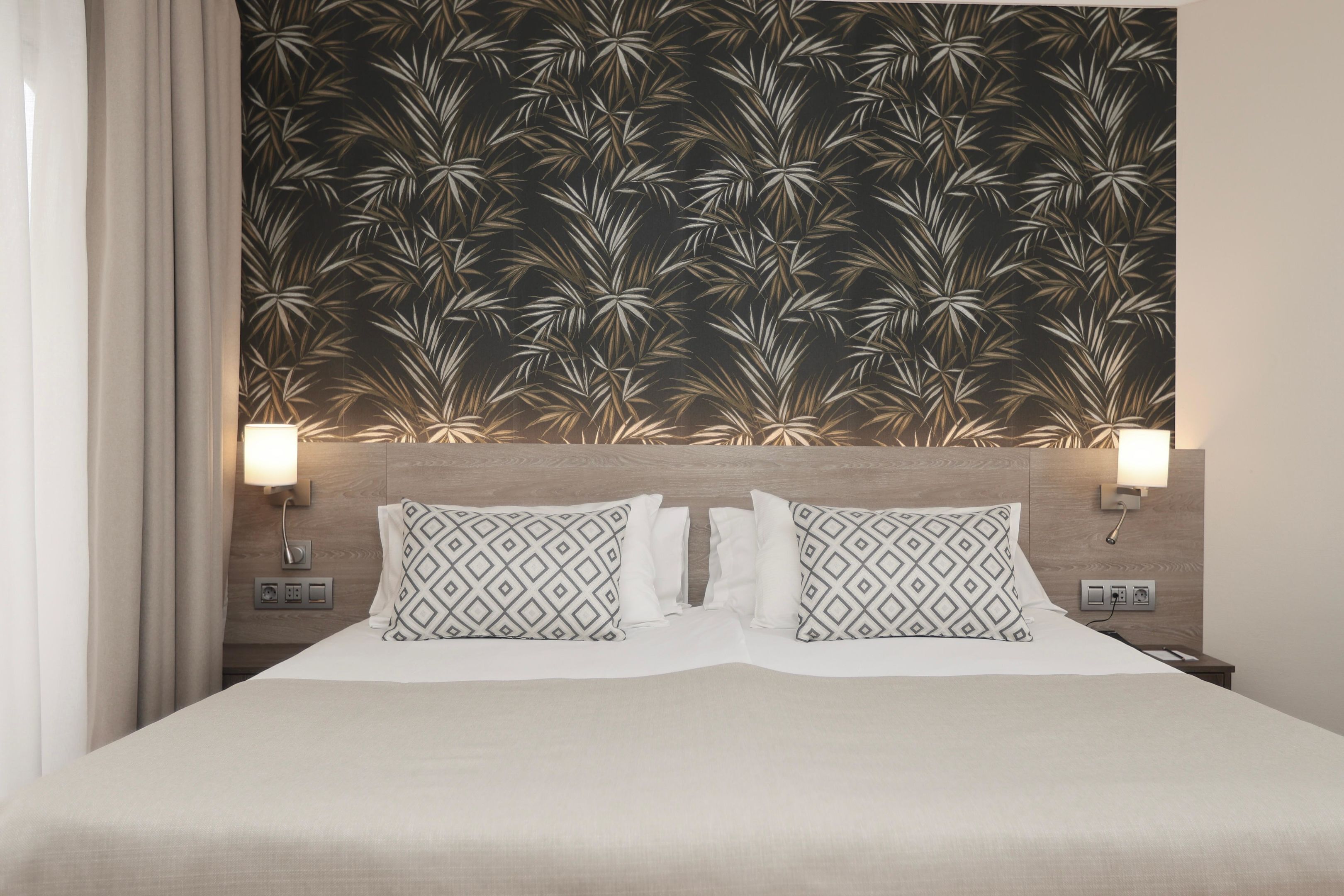 A hotel room with a bed, two bedside lamps, a nightstand, and a wall with a leaf pattern.