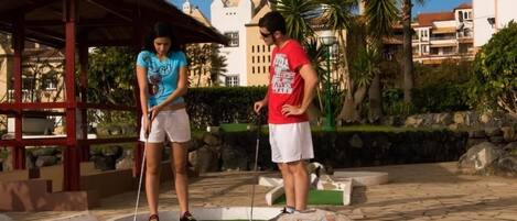 Un campo de mini golf con un pabellón, palmeras y un sendero de piedra.