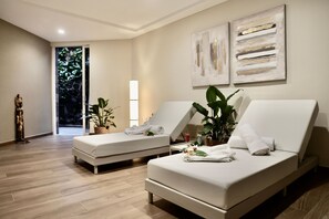 Une chambre moderne avec deux lits blancs, une grande plante en pot et des œuvres d’art abstraites accrochées au mur.