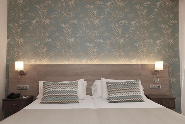 Une chambre d’hôtel avec un grand lit, deux tables de chevet et un mur orné d’un motif de feuilles.