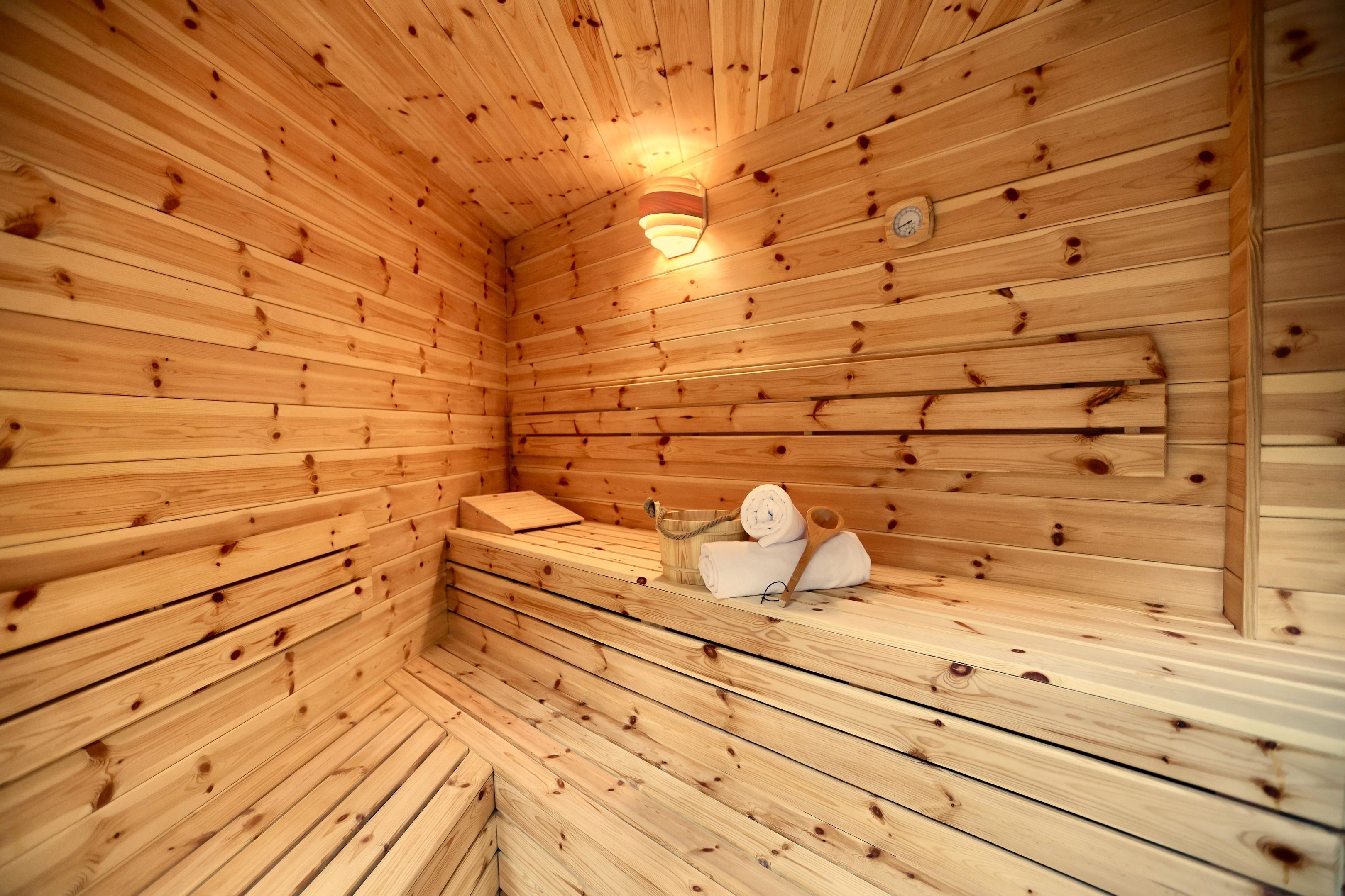 Una sauna de madera con bancos, un perchero para toallas y una lámpara en la pared.