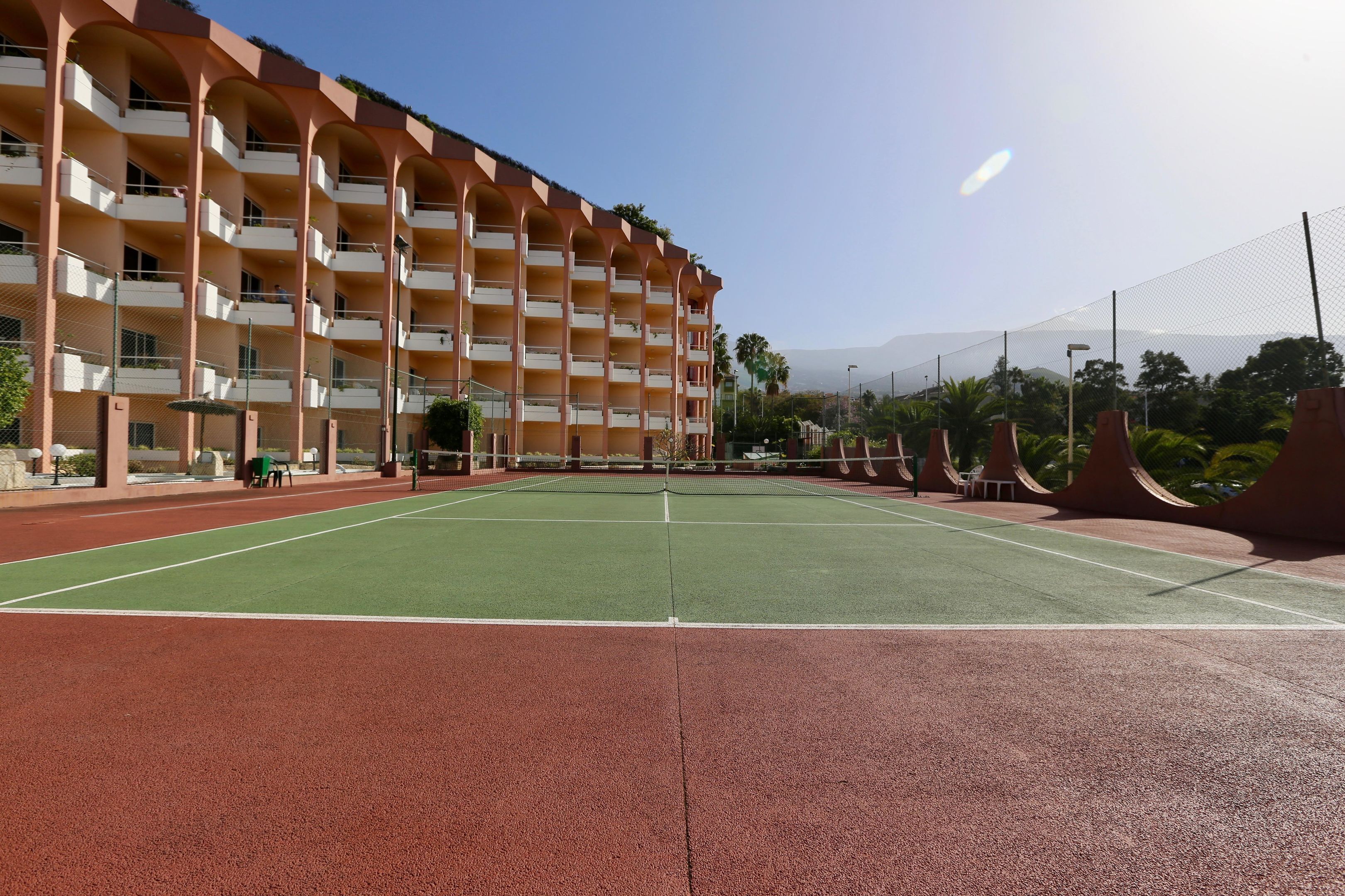 A tennis court adjacent to a multi-story hotel with balconies.