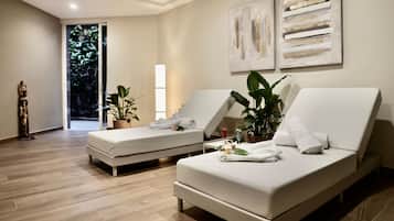 A modern room with two white beds, a large potted plant, and abstract wall art.