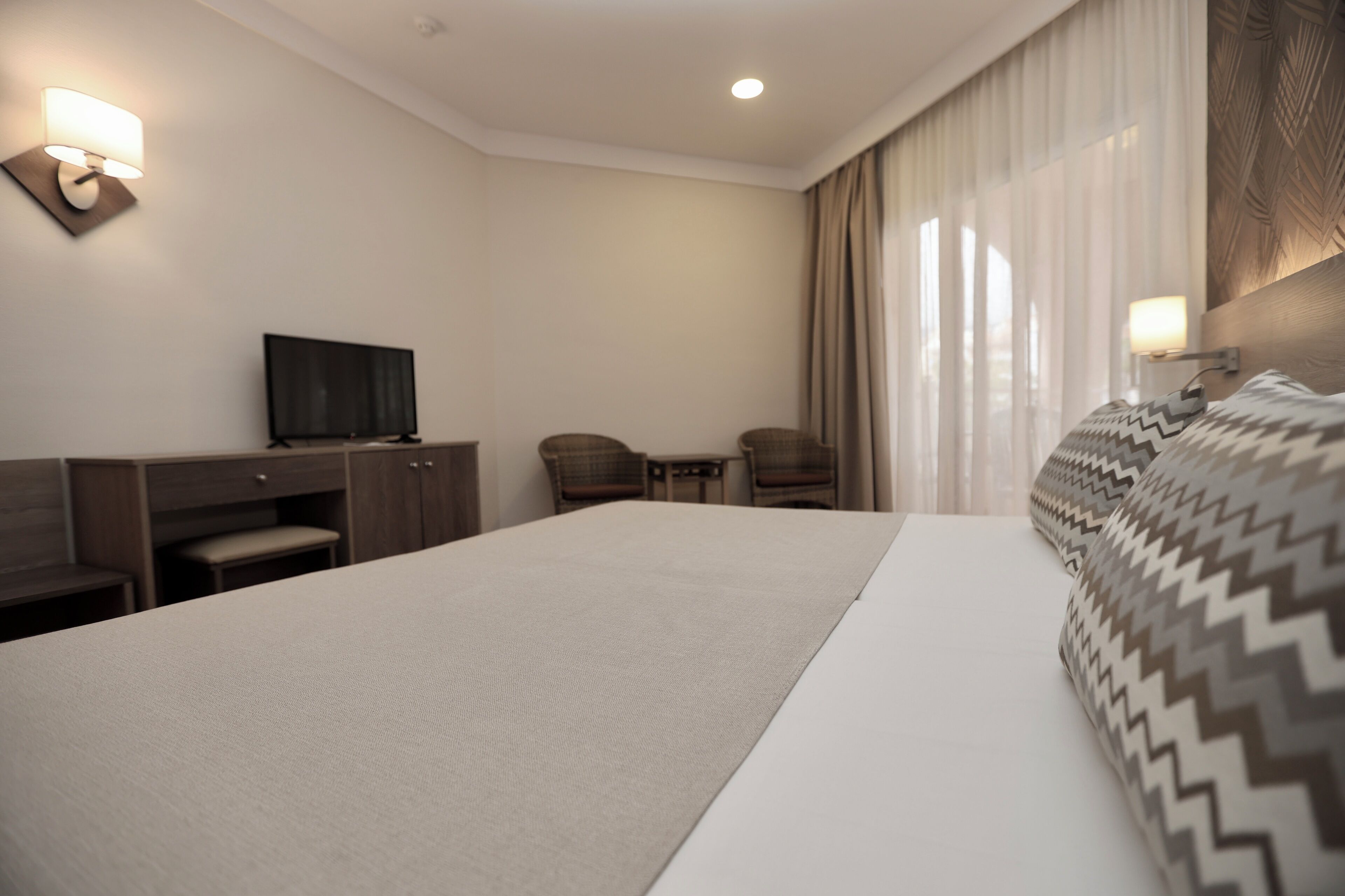 Ein Hotelzimmer mit einem großen Bett, einem Schreibtisch mit Stuhl, einem Fernseher und einem Fenster mit Vorhängen.