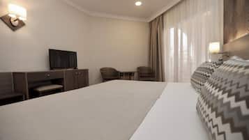 Ein Hotelzimmer mit einem großen Bett, einem Schreibtisch mit Stuhl, einem Fernseher und einem Fenster mit Vorhängen.