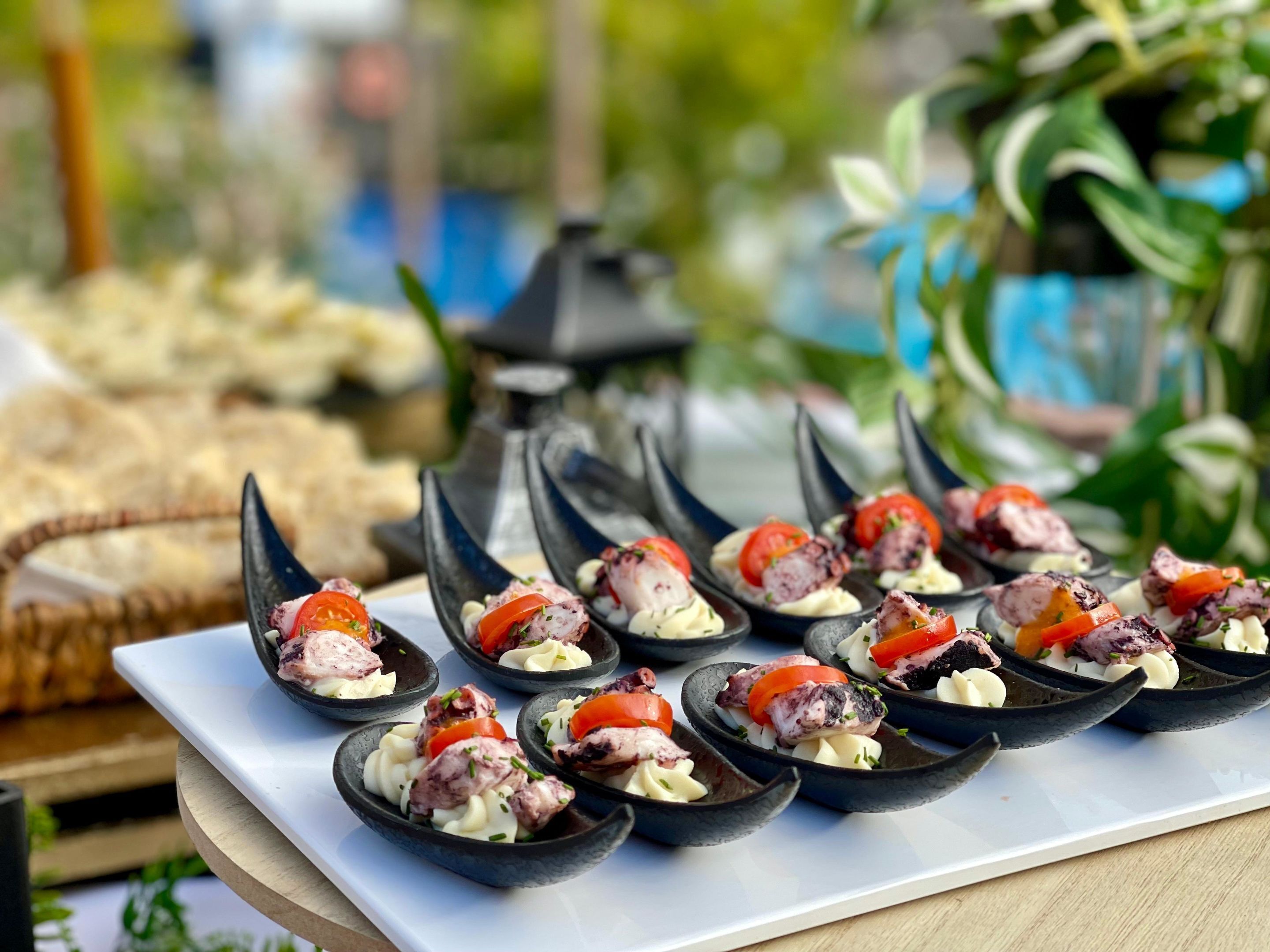 A table with black bowls containing food items, possibly appetizers, with a blurred outdoor background.