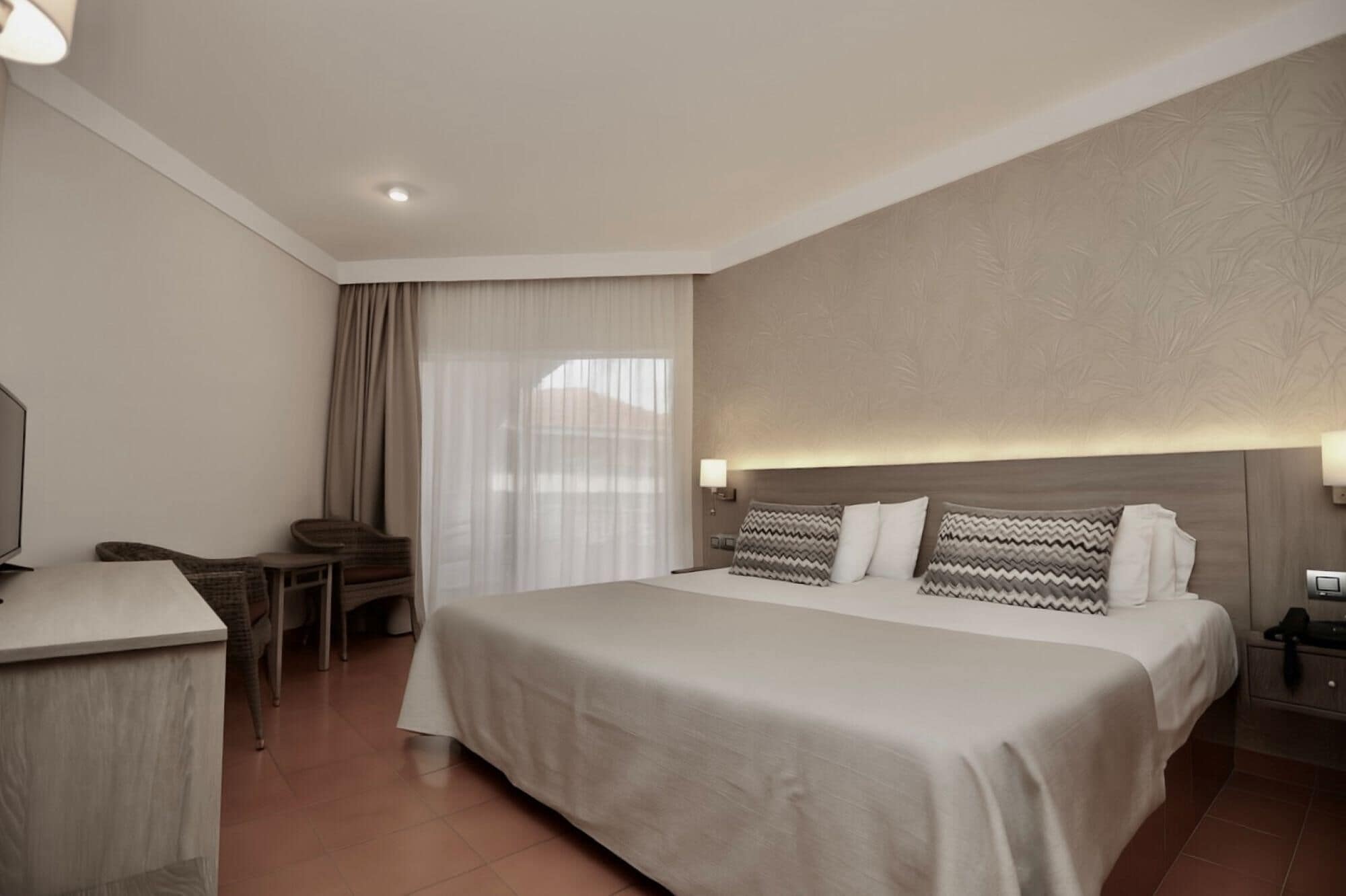 A hotel room with a large bed, a desk, a chair, a TV, and a window with curtains.