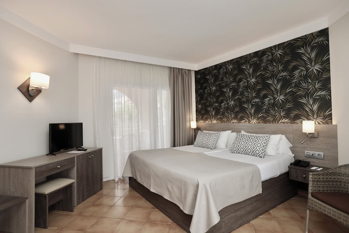 Une chambre d’hôtel moderne, dotée d’un grand lit, d’un bureau, d’une télévision et d’un luminaire fixé au mur.
