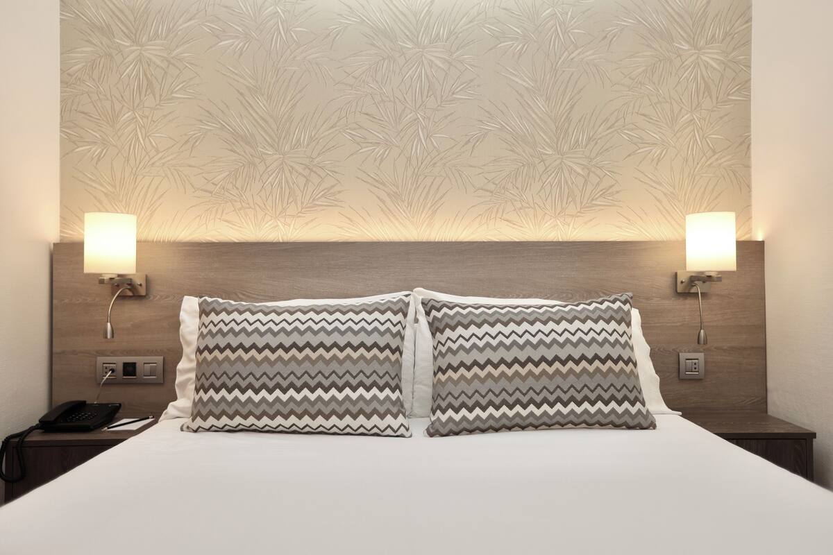 A hotel room with a bed, two nightstands, a phone, and wall-mounted lamps.