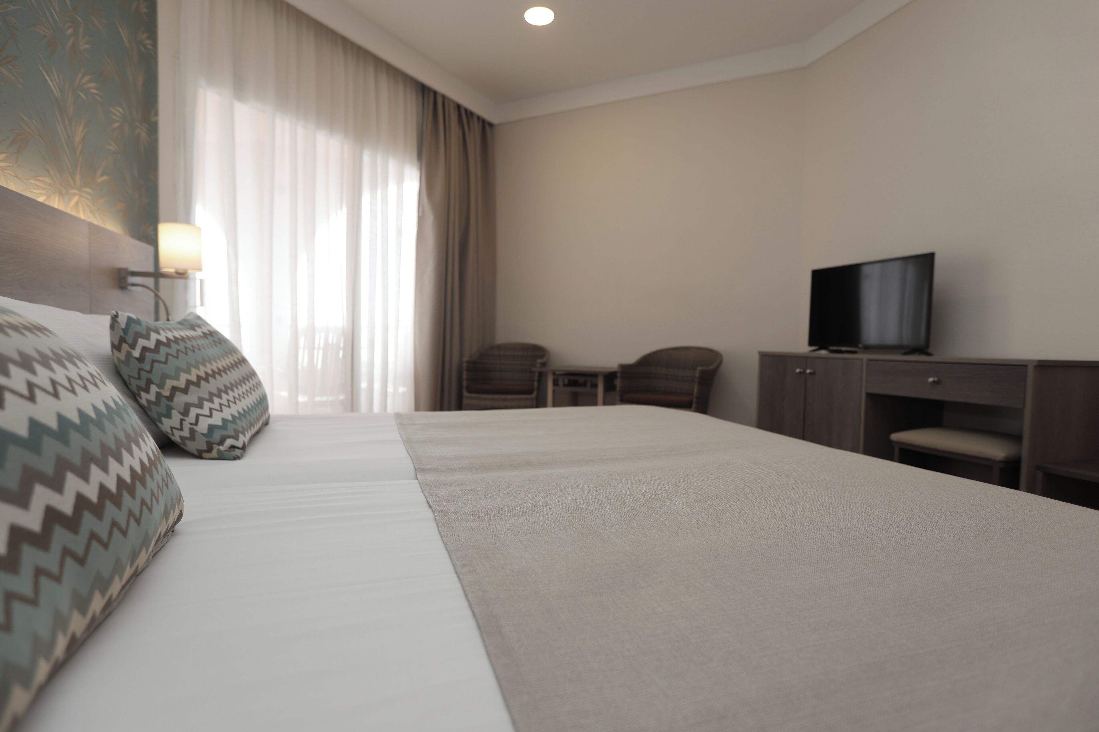A hotel room with a large bed, two chairs, a desk, and a television.