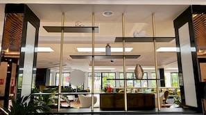 Un intérieur moderne avec un espace salon central, un plafond doté d’un éclairage encastré et une vue sur l’extérieur grâce à de grandes fenêtres.