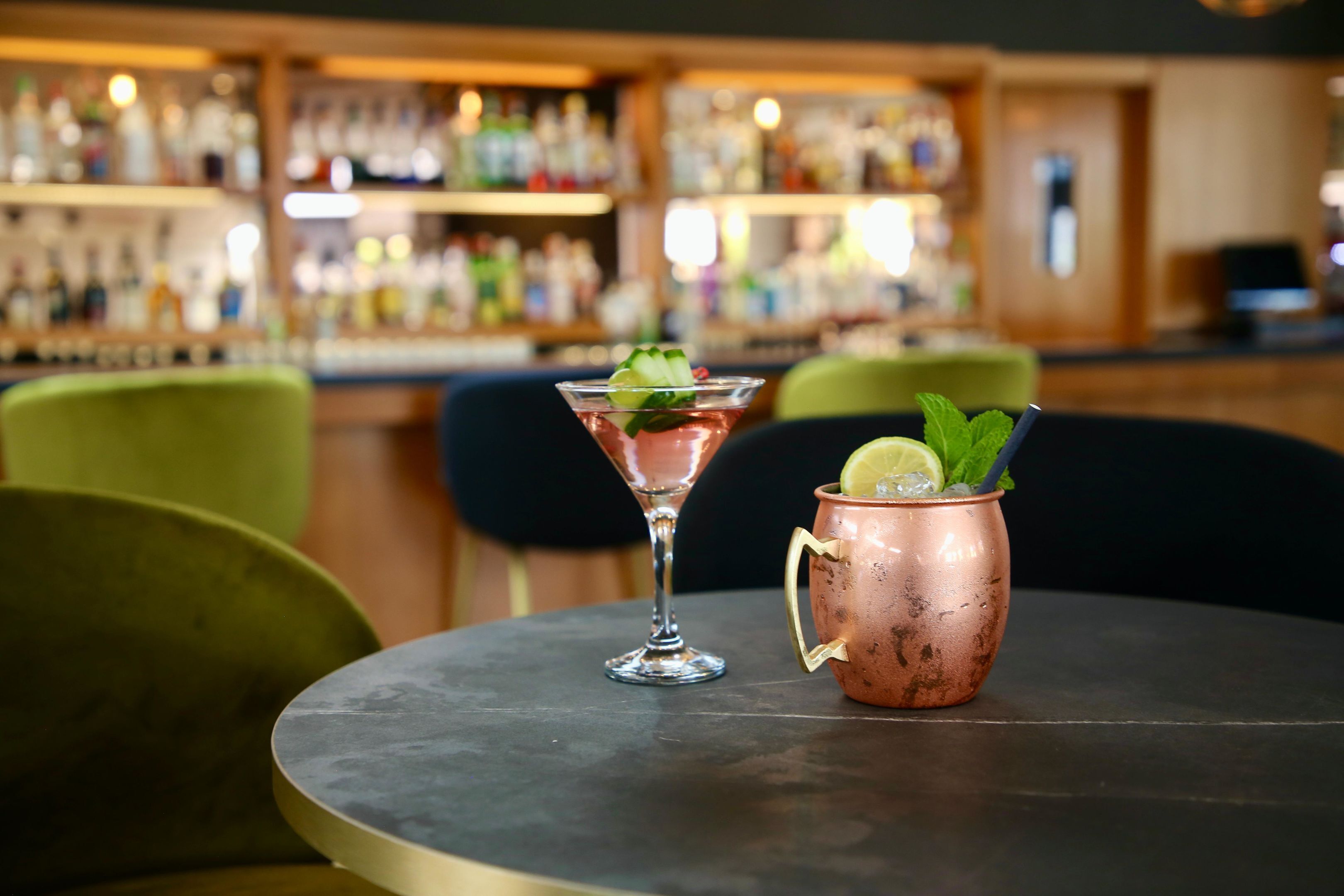 Eine Bar mit einem runden Tisch, zwei Getränken und einer Theke voller Flaschen.