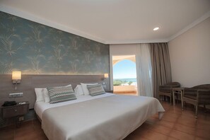 Une chambre d’hôtel avec un grand lit, deux lampes de chevet, une table de chevet, un fauteuil en osier et une vue sur l’extérieur.