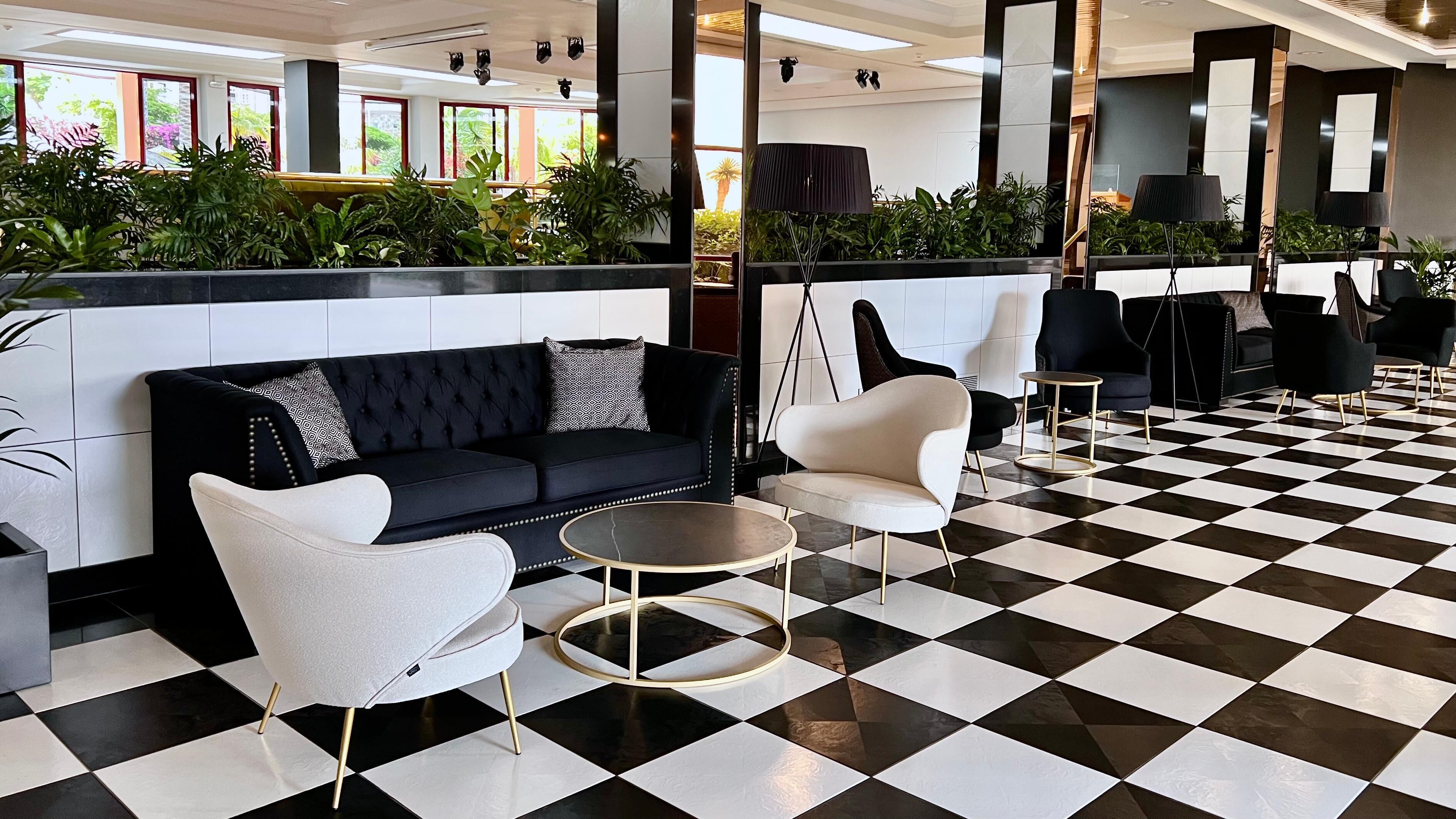 Un vestíbulo con suelo a cuadros blanco y negro, un sofá negro con cojines estampados y sillones blancos.