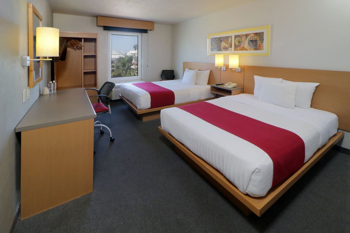 A hotel room with two beds, a desk, a chair, and a window with a view.