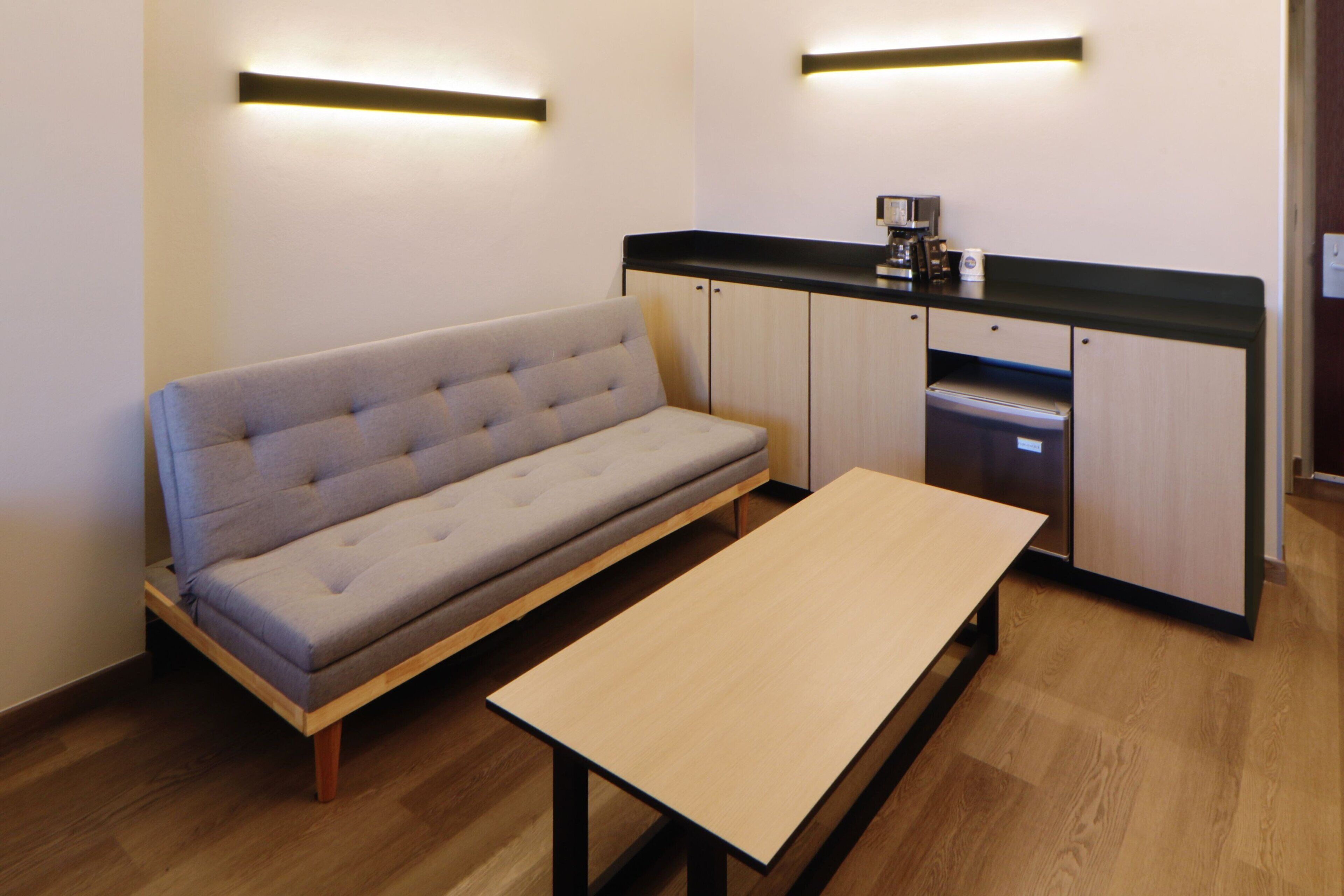 Una kitchenette moderna con horno empotrado y microondas, un sofá gris y una mesa de madera.