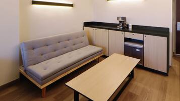 Una kitchenette moderna con horno empotrado y microondas, un sofá gris y una mesa de madera.