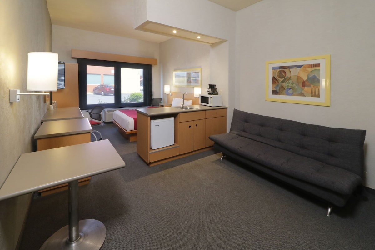 A compact hotel room with a kitchenette, a sofa, a desk, and a bed.