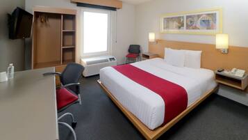 Hotelkamer met een bed, bureau, stoel, kledingkast, televisie, raam en een schilderij aan de muur.