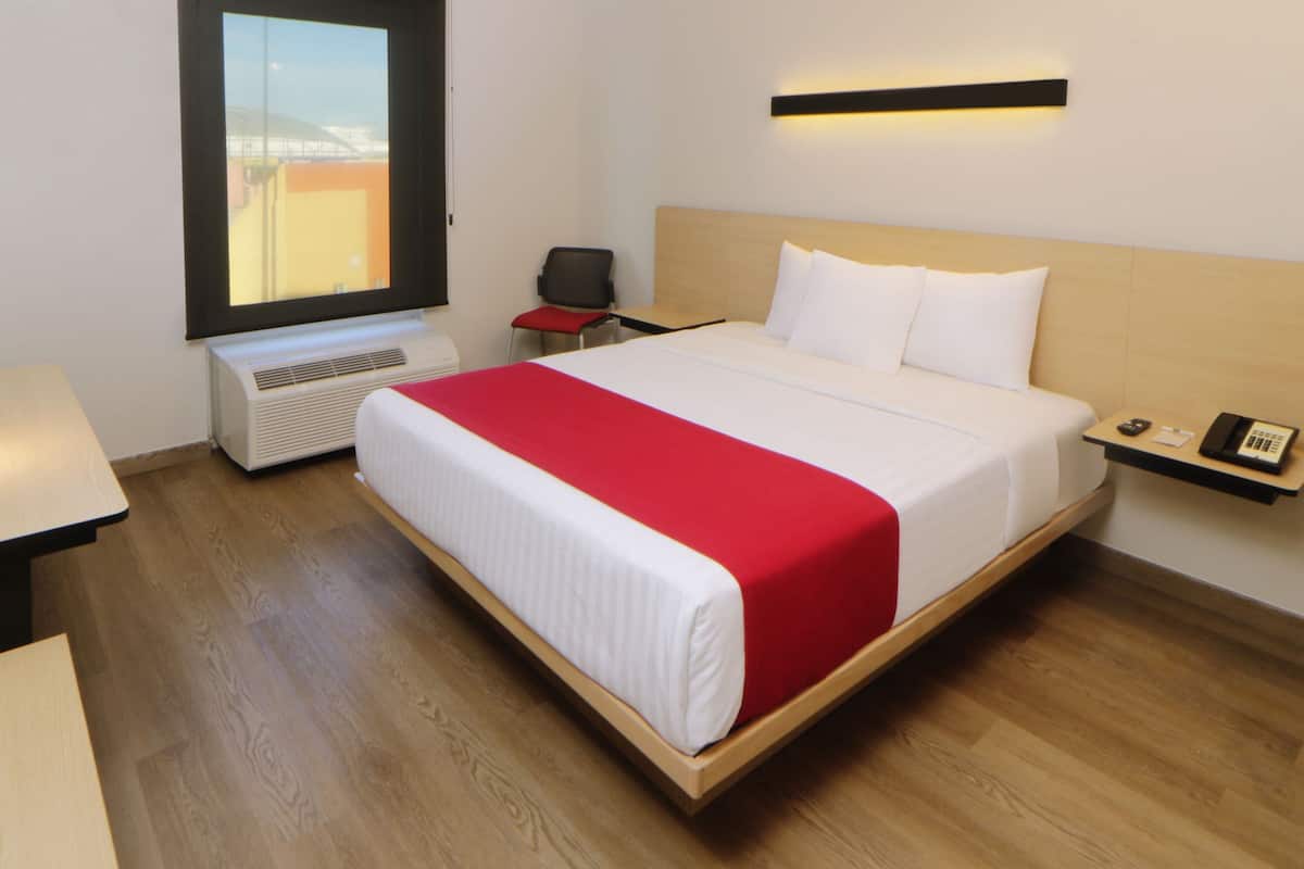 A hotel room with a bed, a desk, a chair, a window, and a wall-mounted phone.