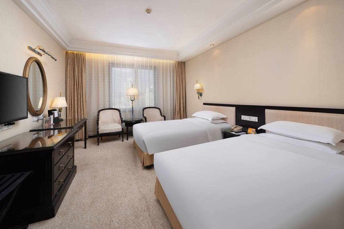 Une chambre d’hôtel avec deux lits, un bureau avec une télévision, un miroir et deux chaises.