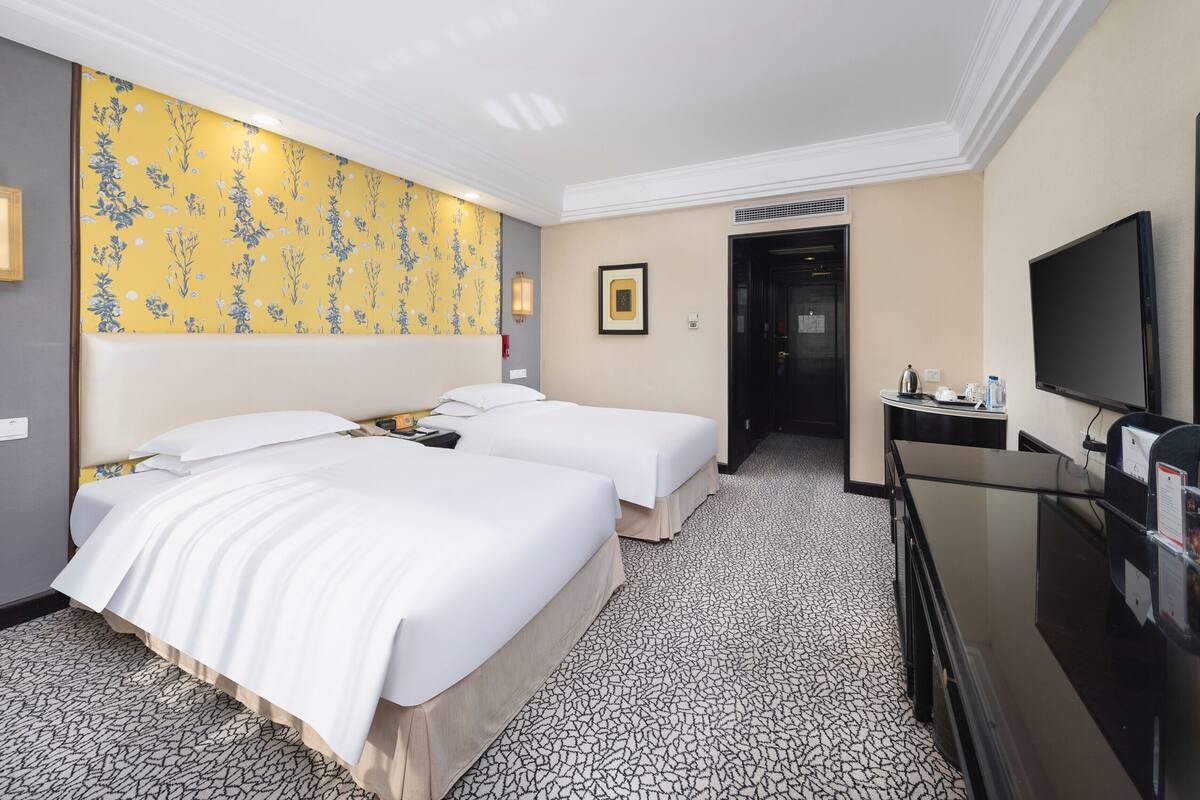 Une chambre d’hôtel avec deux lits, une télévision, un bureau et une porte de salle de bain.