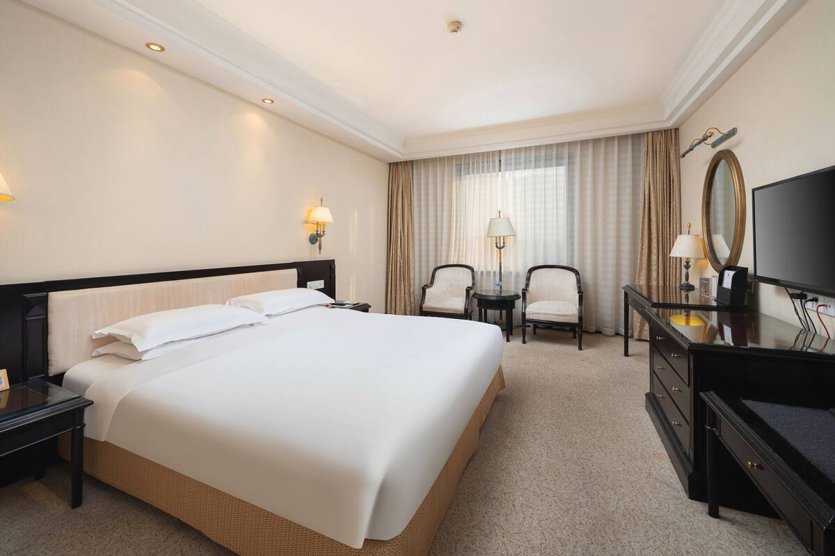 Une chambre d’hôtel avec un grand lit, un bureau avec une chaise, une télévision et une lampe.