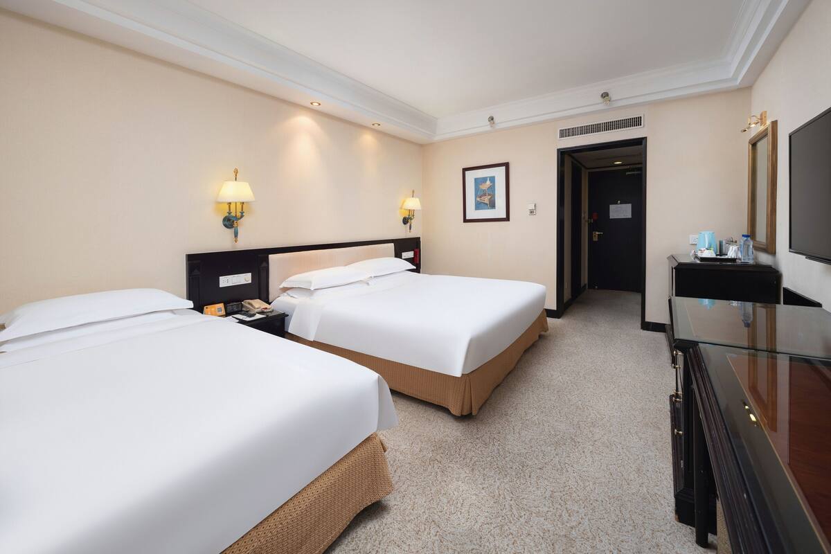 Une chambre d’hôtel avec deux lits, un bureau, une commode et un téléviseur.