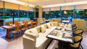 A modern dining area with a long table, cushioned seating, and large windows offering a view of the outdoors. - Grand Metropark Hotel Hangzhou (Hangzhou)