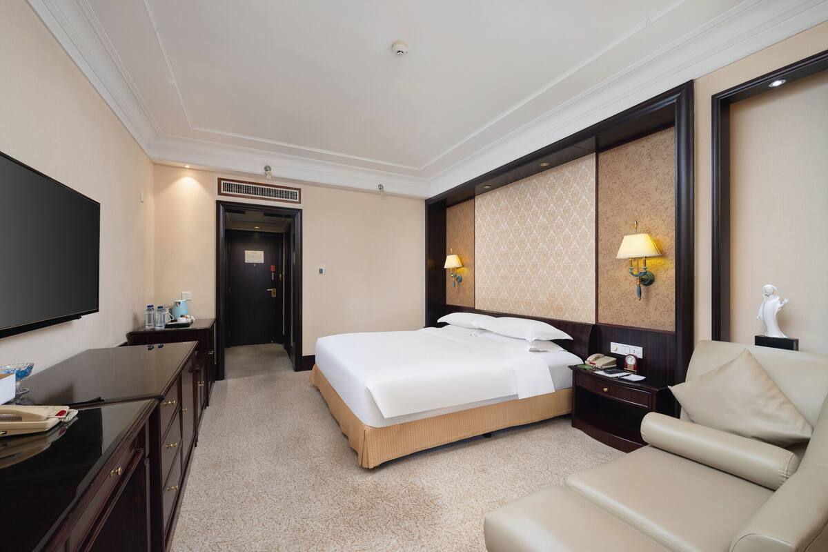 Une chambre d’hôtel équipée d’un lit, d’un bureau, d’une chaise, d’une télévision et d’une lampe fixée au mur.