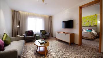 Hotelkamer met een bank, twee fauteuils, een salontafel, een televisie, een kast en een bed met bloemenbehang.