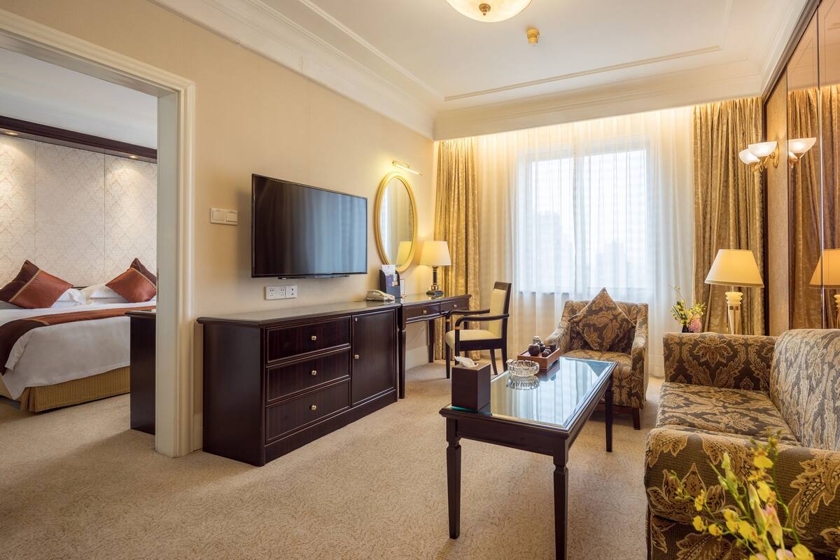 Une chambre d’hôtel avec un lit, un bureau, un canapé, une télévision et une grande fenêtre avec des rideaux.