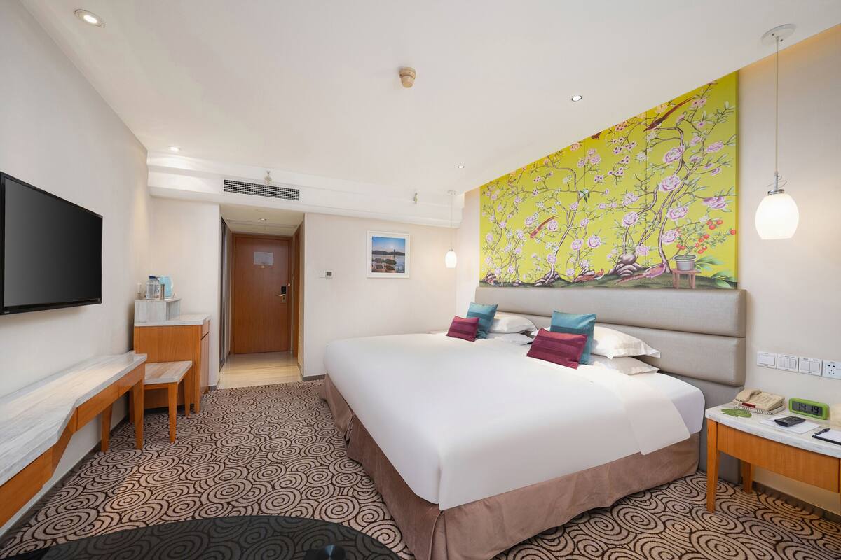 Une chambre d’hôtel avec un grand lit, un bureau, une chaise, une télévision et un tableau au mur.