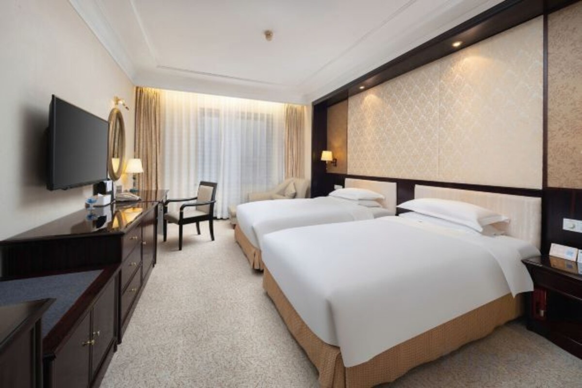 Une chambre d’hôtel avec deux lits, un bureau avec une chaise, une télévision et une grande fenêtre avec des rideaux.