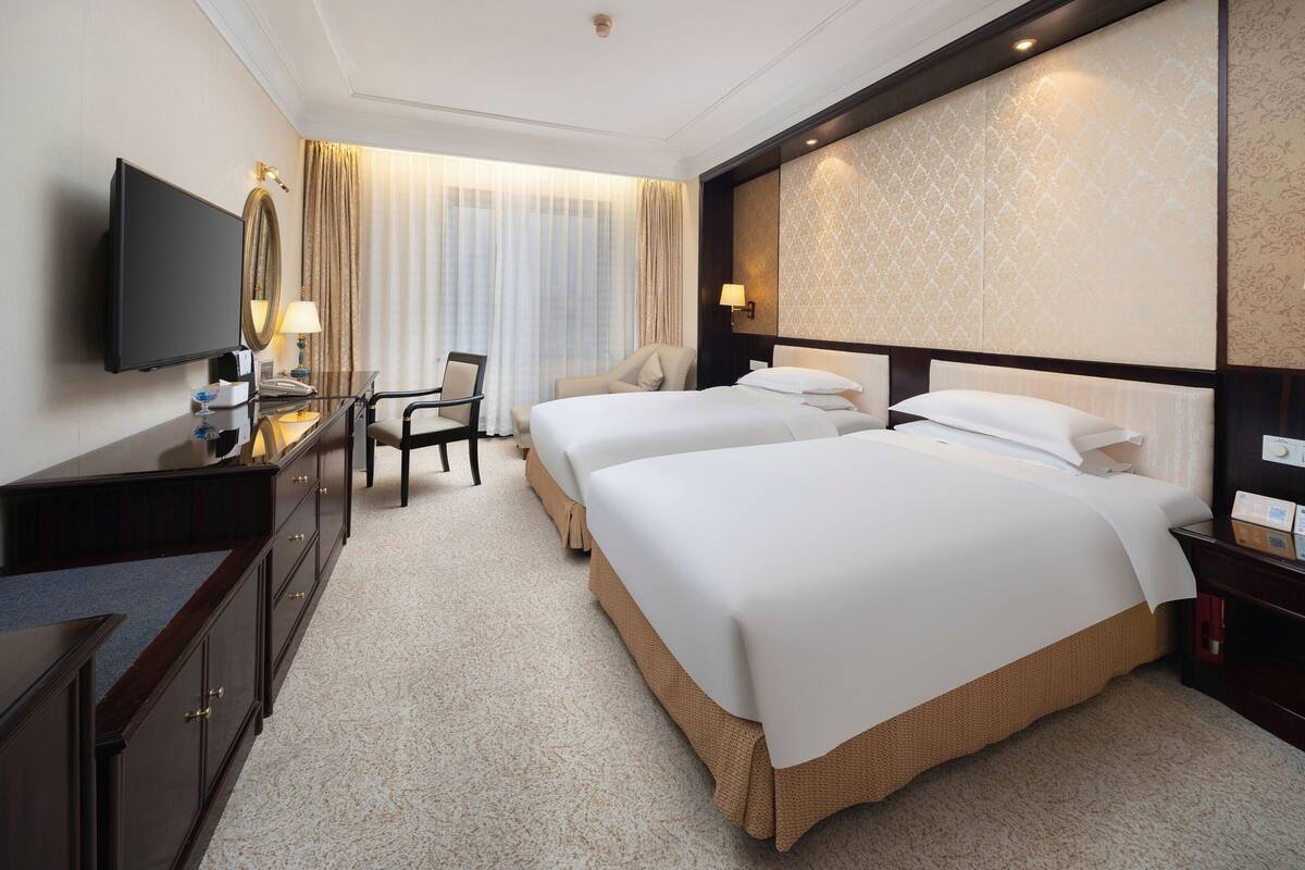 Une chambre d’hôtel avec deux lits, un bureau avec une télévision, une chaise et un grand miroir.