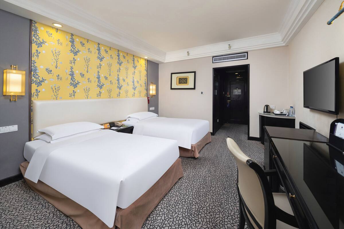 Une chambre d’hôtel avec deux lits, un bureau, une chaise, une télévision et une porte de salle de bain.