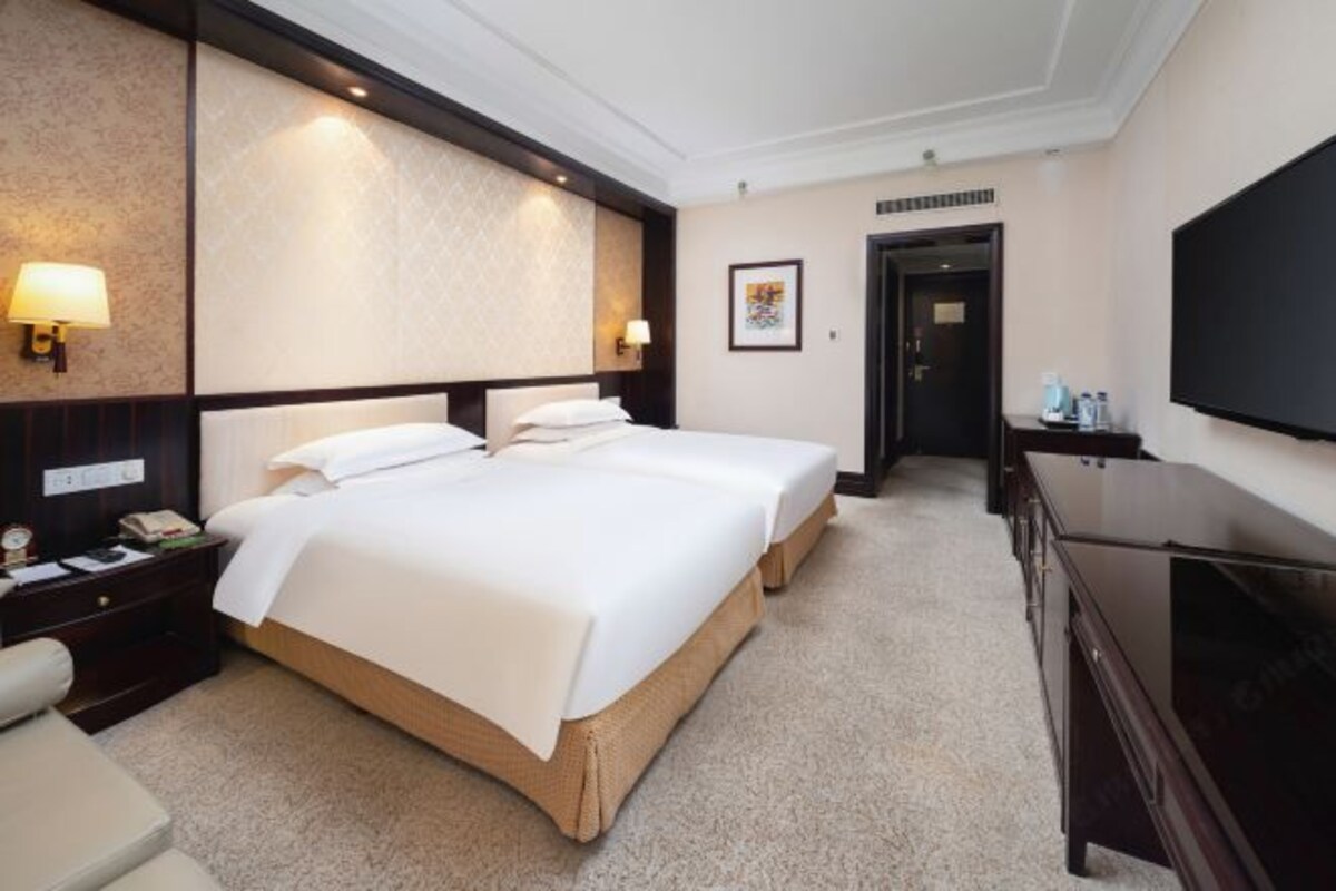Ein Hotelzimmer mit zwei Betten, einem Schreibtisch mit Lampe, einem Schminktisch und einem Flachbildfernseher.