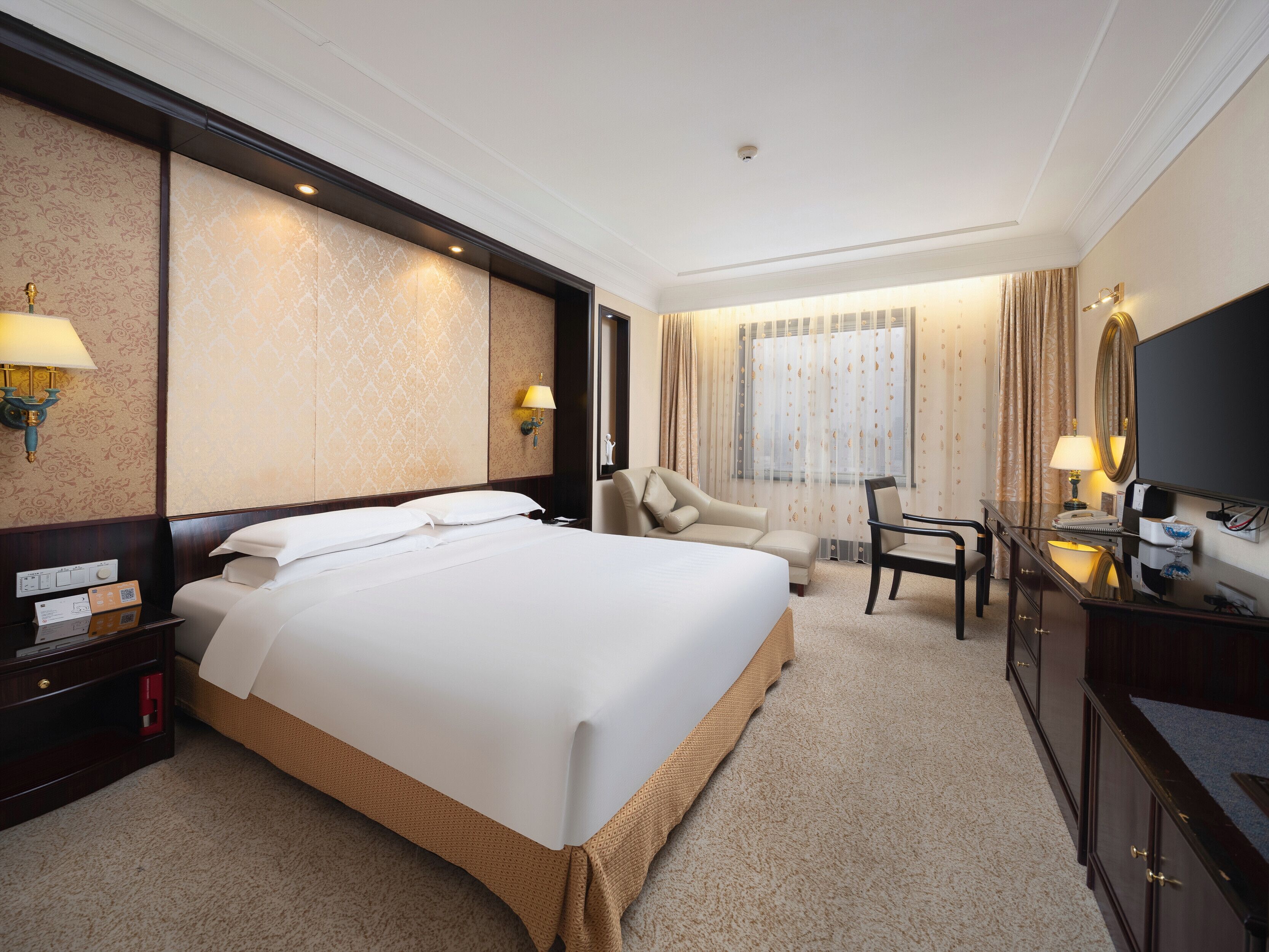 A hotel room with a large bed, a desk with a chair, a television, and a window with curtains.