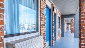 A corridor with brick walls, blue doors, and a window with blinds. - SureStay Hotel by Best Western Oklahoma City West (Oklahoma City)
