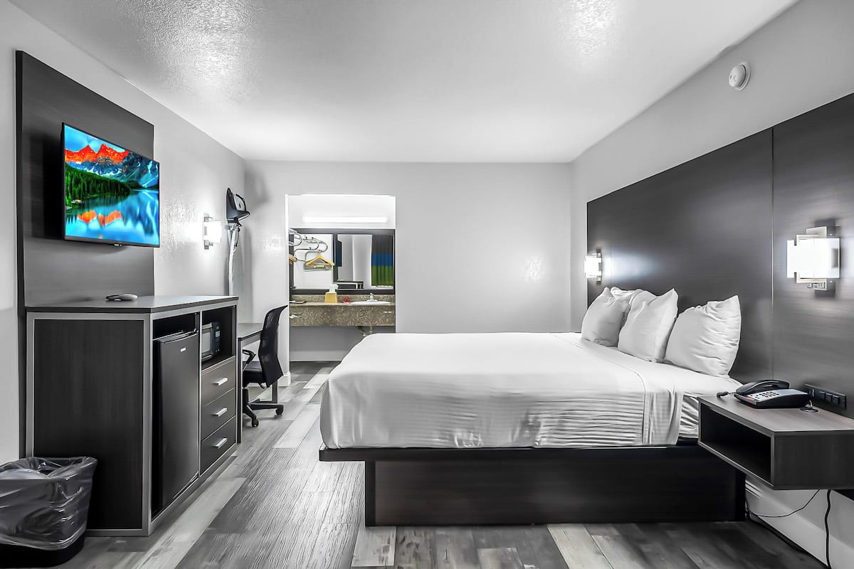 Ett modernt hotellrum med en stor säng, ett skrivbord och en TV som är monterad på väggen.