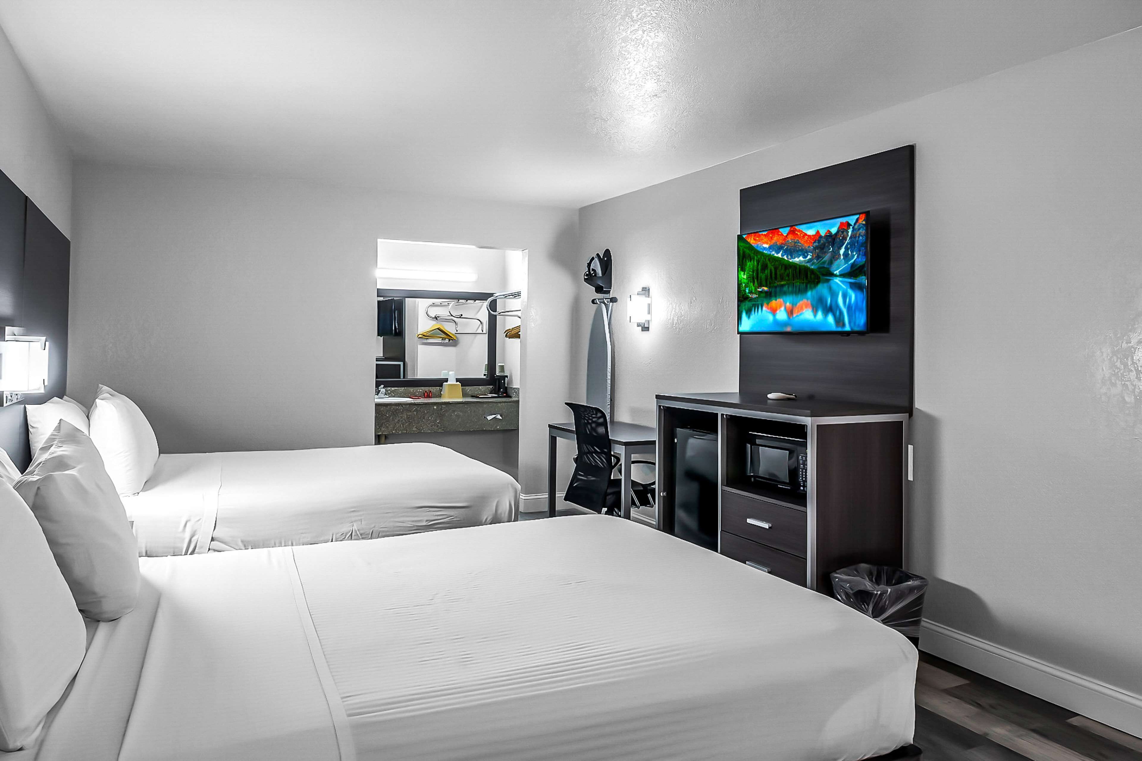 A hotel room with two beds, a TV mounted on the wall, a desk with a chair, and a mirror.