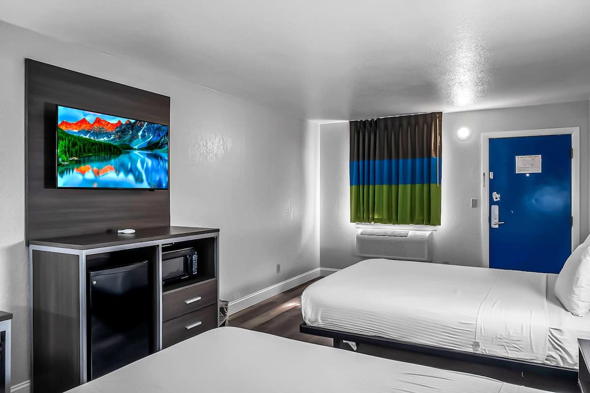 Ett hotellrum med en säng, en tv som är monterad på väggen, ett skrivbord med en mikrovågsugn och en blå dörr.